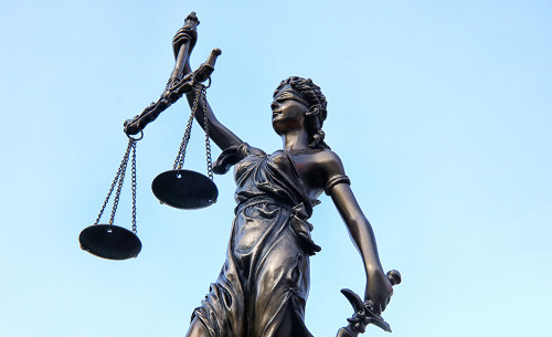 Eine Justitia-Statue vor dem blauen Himmel.