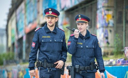 Eine Polizistin spricht in ihr Funkgerät, ihr Kollege geht neben ihr.